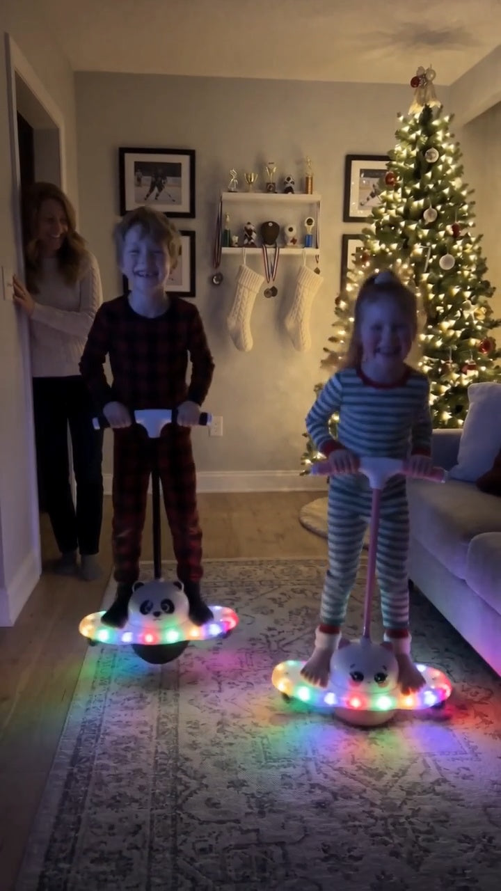 Brother and sister bouncing on their glowing Pogo Glow jumpers with the lights off